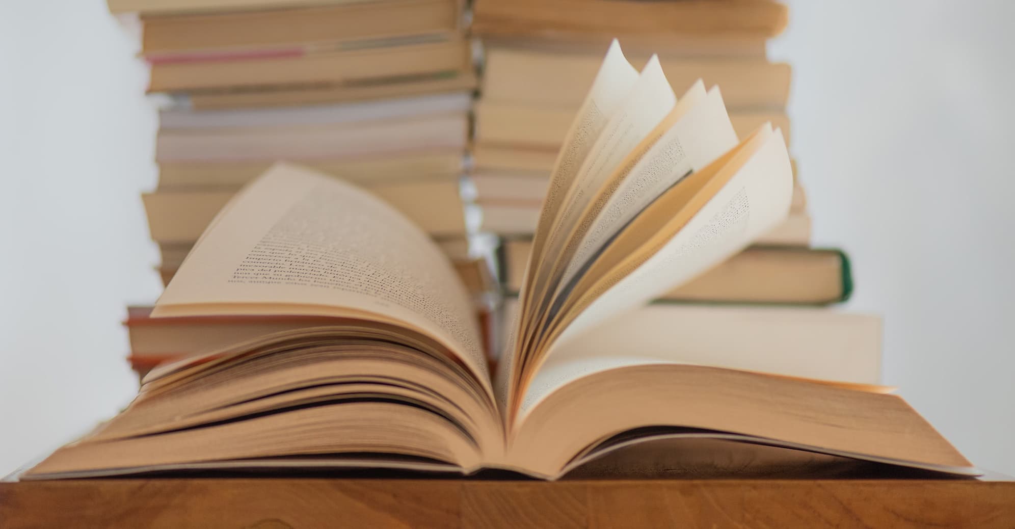 An open book with its pages splayed, in front of two stacks of books.