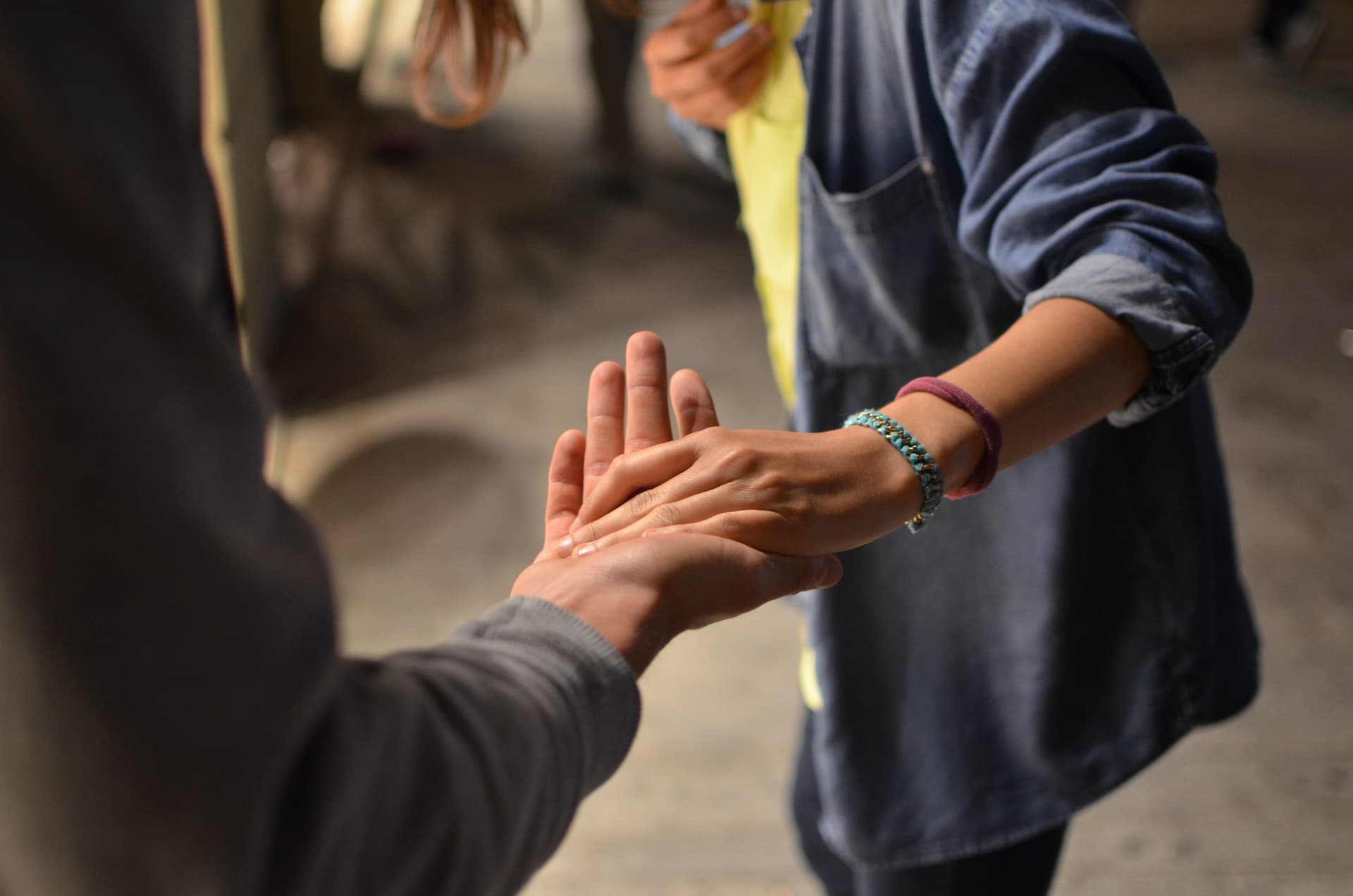 A person in a blue textured coat placing their hand in another's hand.