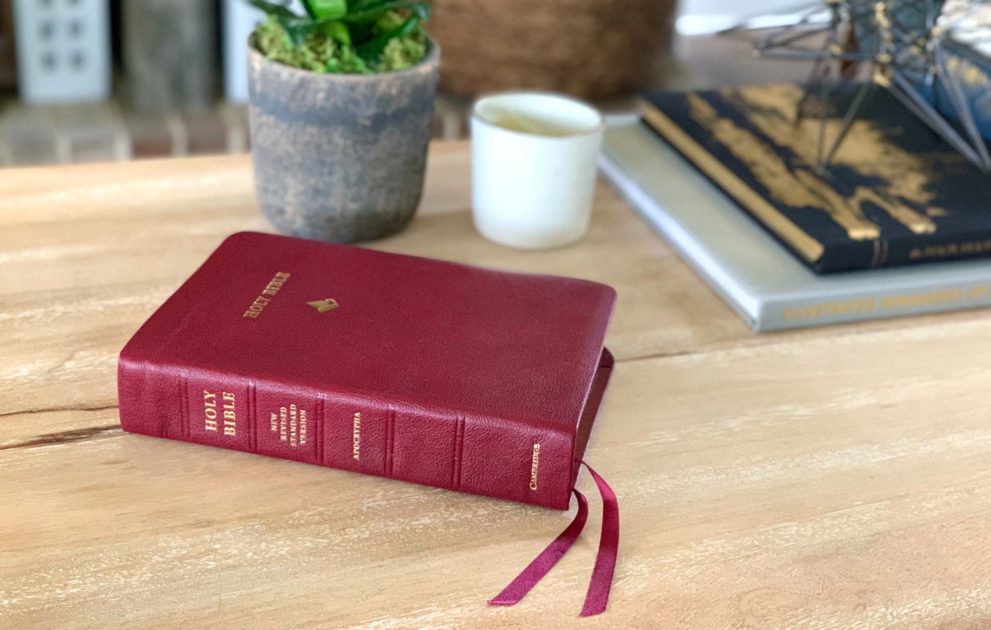 A red Bible laying on a wooden table with a decorative plant and other knick knacks.