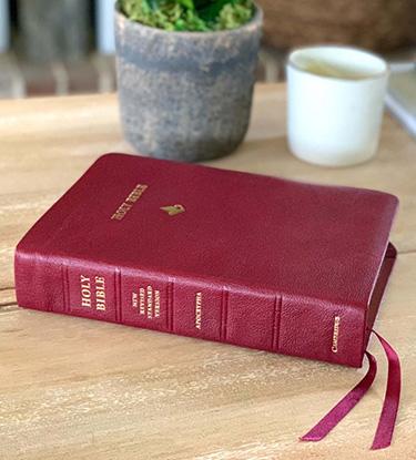A red Bible laying on a wooden table.